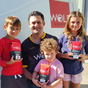 Family of four holding Wolf coffee bags in front of a Wolf Coffee sign.