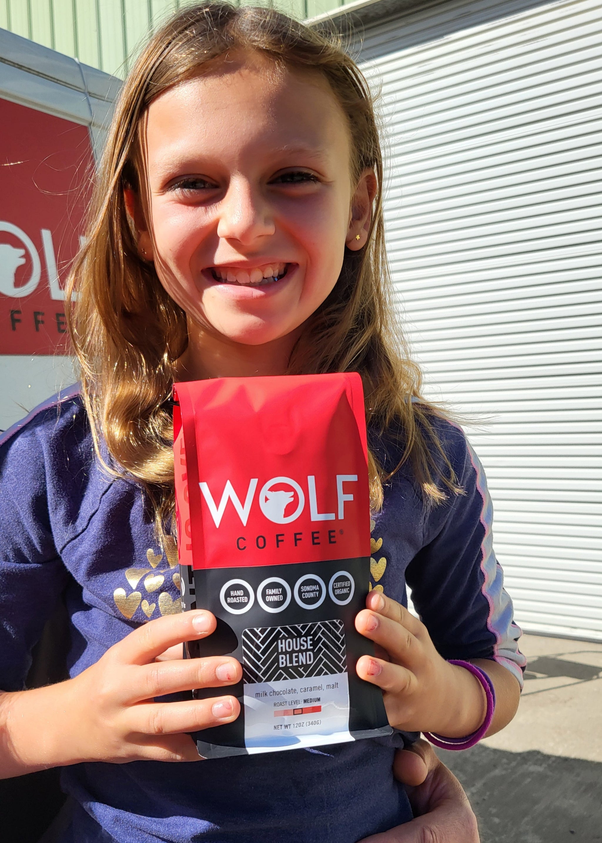 Child holding a red and black product with 'WOLF' branding in front of a building.