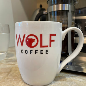 White mug with 'Wolf Coffee' logo in front of a coffee machine.